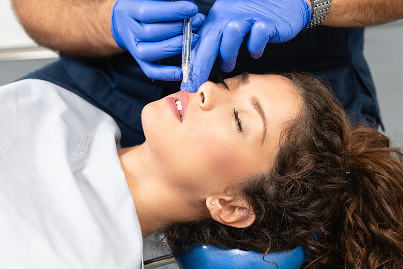 Une professionnelle en soins esthétique de la clinique Belladerma Dix30 située à Brossard, effectuant une injection d'agent de comblement sur la lèvre supérieure d'une patiente 