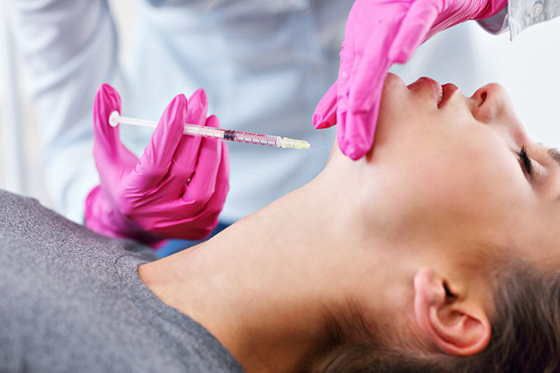 Une professionnelle en soins esthétique effectuant une injection de Belkyra sous le menton d'une patiente pour améliorer l'apparence et le profil de la graisse modérée à sévère sous le menton